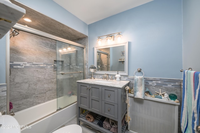 full bath featuring toilet, a wainscoted wall, combined bath / shower with glass door, vanity, and tile walls