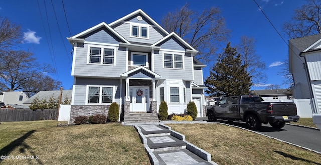 view of front facade featuring stone siding, a front yard, and fence