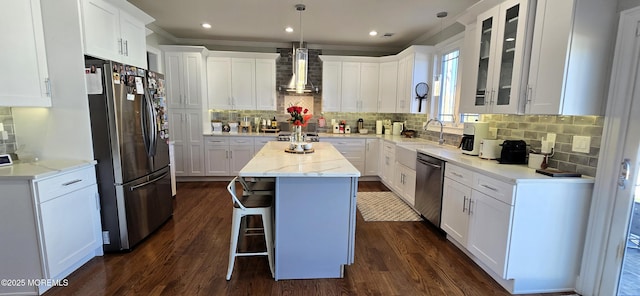 kitchen featuring white cabinets, wall chimney exhaust hood, a center island, stainless steel appliances, and a sink