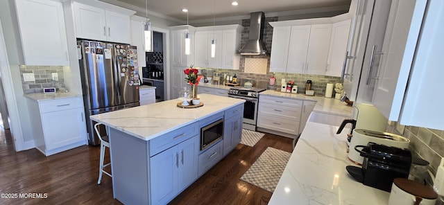 kitchen with dark wood finished floors, a kitchen island, appliances with stainless steel finishes, ornamental molding, and wall chimney range hood