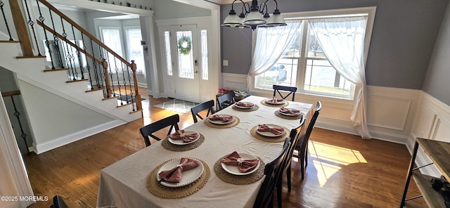 dining room featuring stairway, wainscoting, wood finished floors, and a notable chandelier