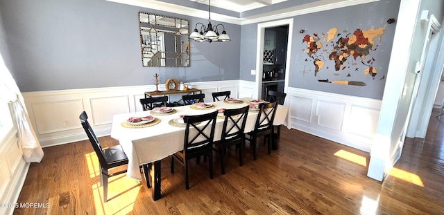 dining space with dark wood-style floors, ornamental molding, a notable chandelier, and a wainscoted wall