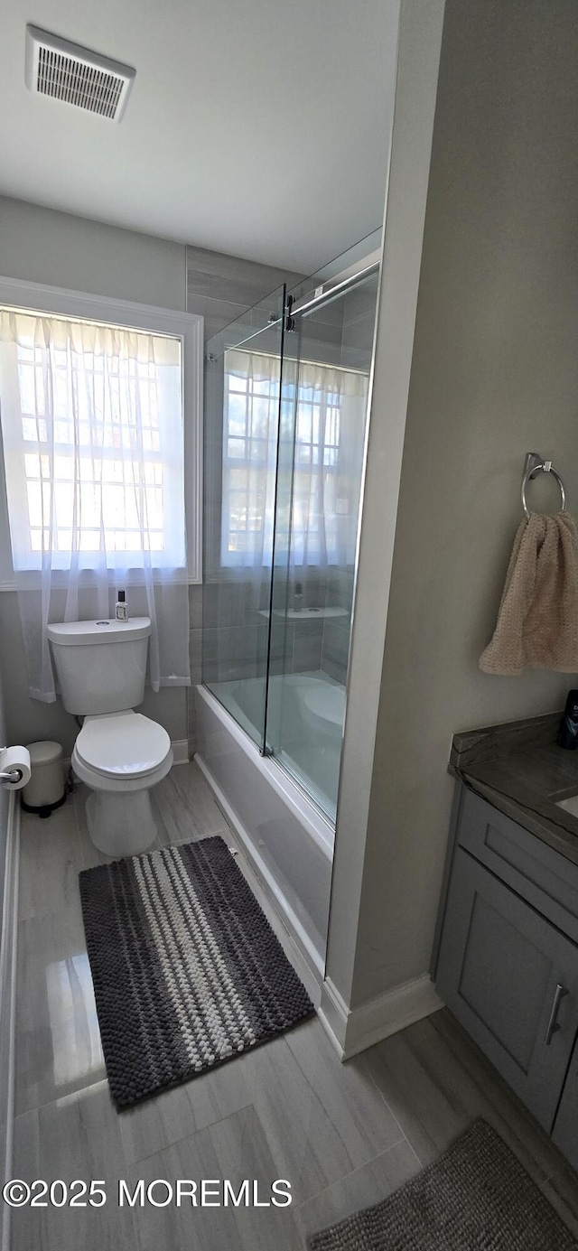 full bathroom with toilet, vanity, visible vents, baseboards, and combined bath / shower with glass door