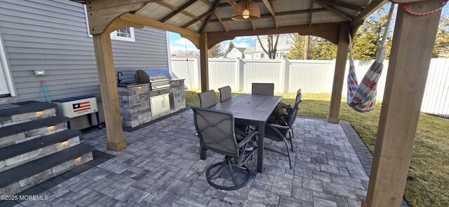 view of patio / terrace featuring an outdoor kitchen, a fenced backyard, a grill, a gazebo, and outdoor dining space