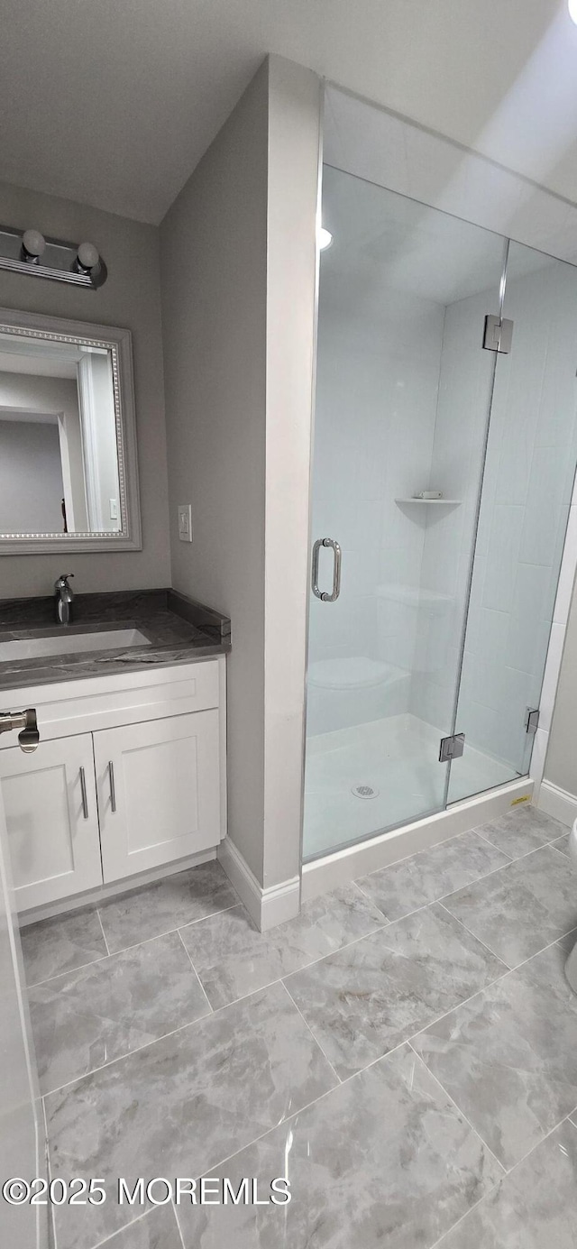 full bath featuring a stall shower, vanity, and baseboards