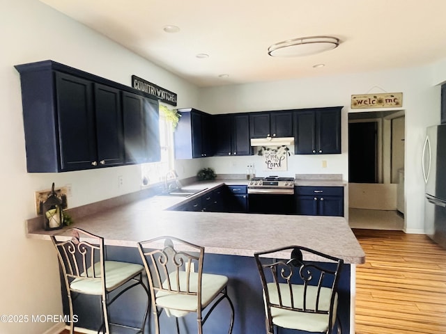 kitchen with a breakfast bar area, light countertops, a peninsula, stainless steel appliances, and a sink