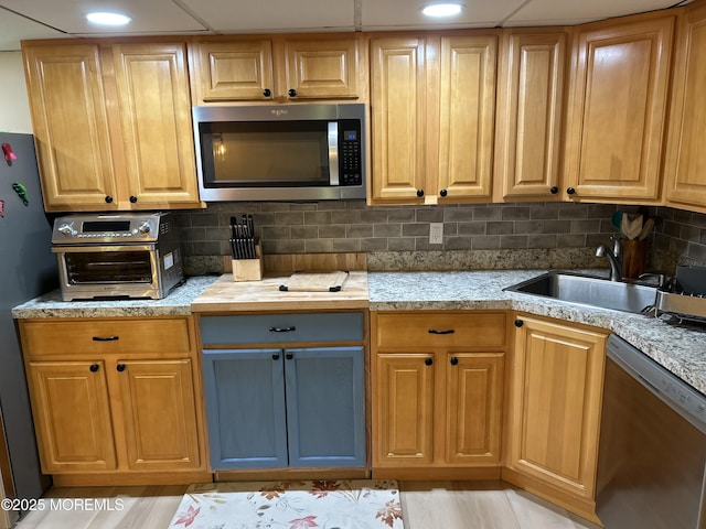 kitchen with light stone counters, a toaster, a sink, stainless steel appliances, and tasteful backsplash