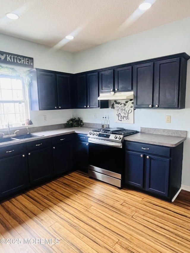 kitchen with stainless steel gas range oven, under cabinet range hood, light wood-style floors, a textured ceiling, and a sink