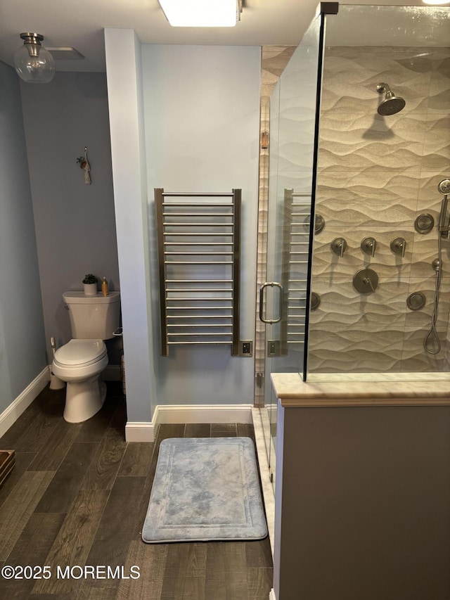 full bath featuring radiator, baseboards, wood finish floors, a stall shower, and toilet