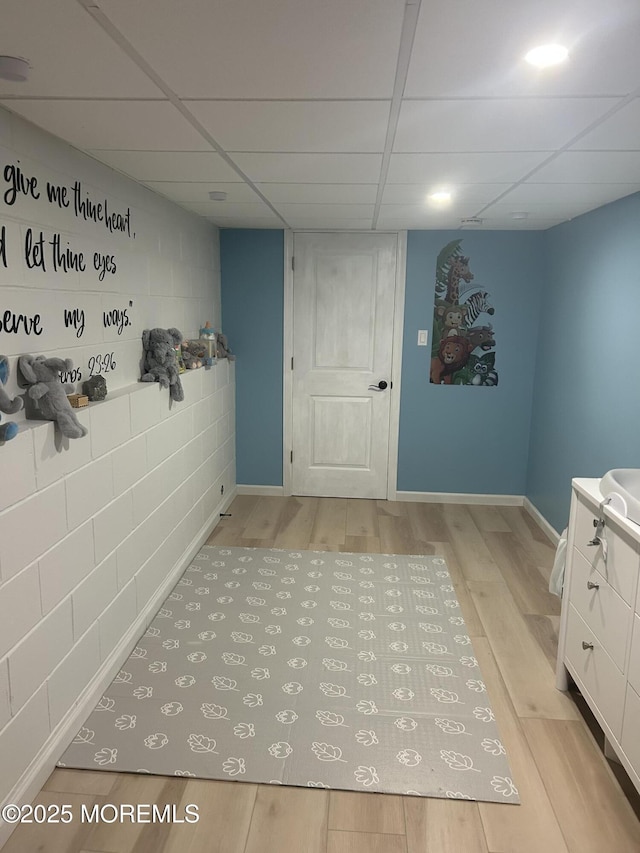 hallway with light wood finished floors, a drop ceiling, and baseboards