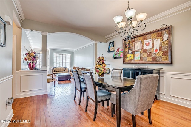 dining area with arched walkways, light wood-style floors, crown molding, and ornate columns