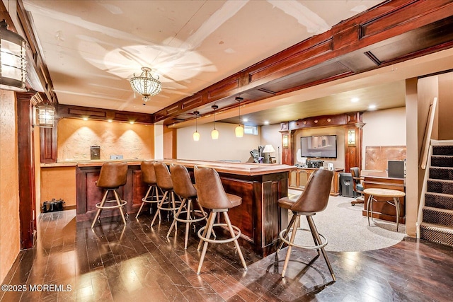 bar with dark wood finished floors, wet bar, and stairs