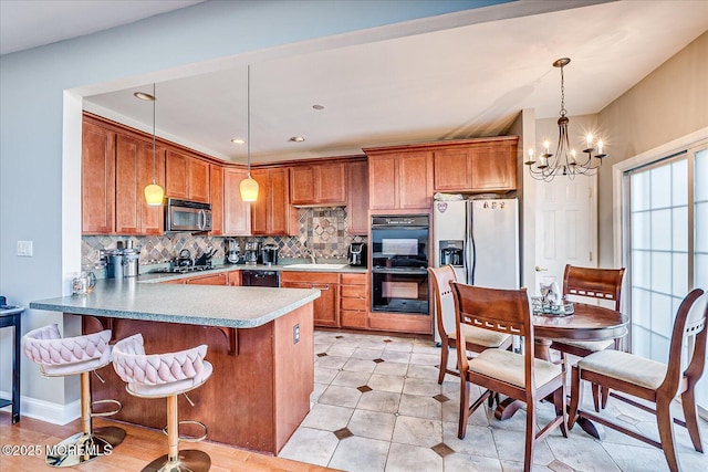 kitchen with brown cabinetry, a peninsula, dobule oven black, stainless steel microwave, and tasteful backsplash