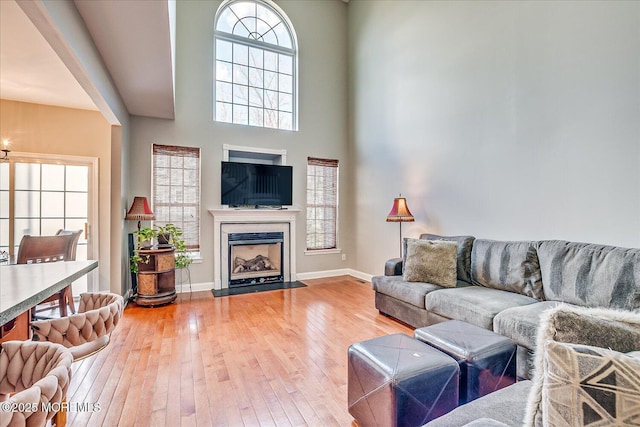 living room with a high ceiling, a fireplace, light wood-type flooring, and baseboards