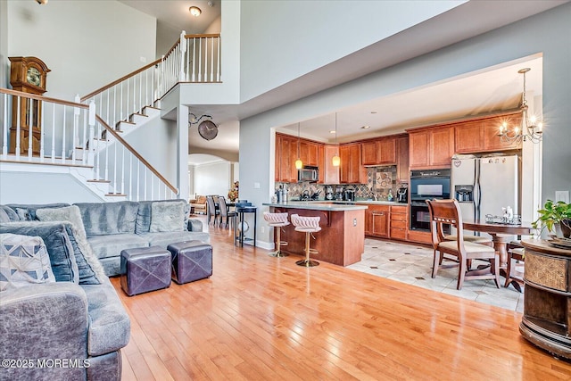 living room featuring stairway, a high ceiling, arched walkways, a notable chandelier, and light wood-type flooring