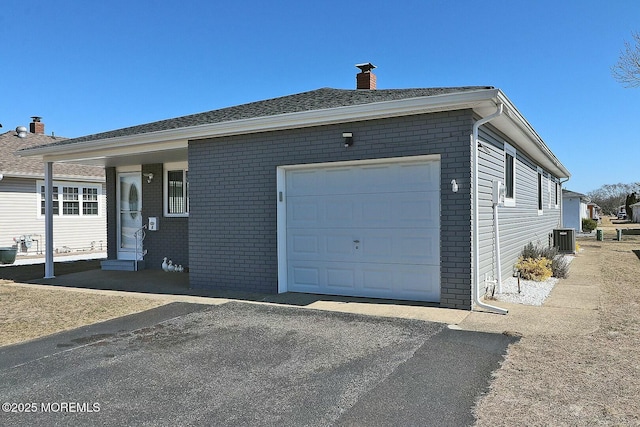 exterior space with central air condition unit, a garage, brick siding, and driveway