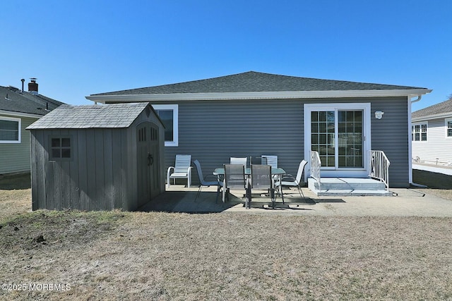 back of property featuring a patio area, a storage shed, a shingled roof, and an outbuilding