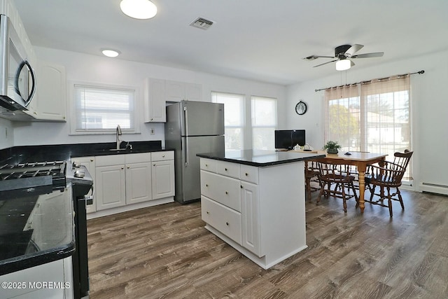 kitchen featuring dark wood-type flooring, a sink, dark countertops, a center island, and stainless steel appliances