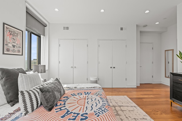 bedroom with recessed lighting, visible vents, two closets, and wood finished floors