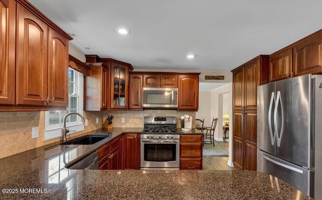 kitchen featuring dark stone counters, a sink, glass insert cabinets, appliances with stainless steel finishes, and backsplash