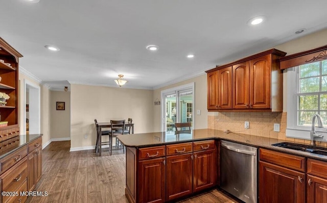 kitchen with wood finished floors, a peninsula, ornamental molding, a sink, and dishwasher