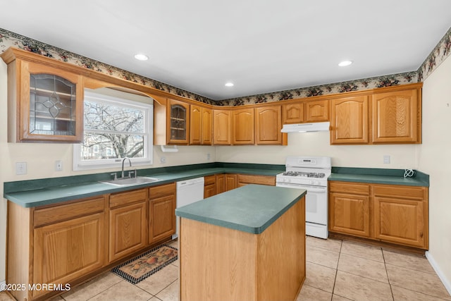 kitchen featuring white appliances, dark countertops, glass insert cabinets, under cabinet range hood, and a sink