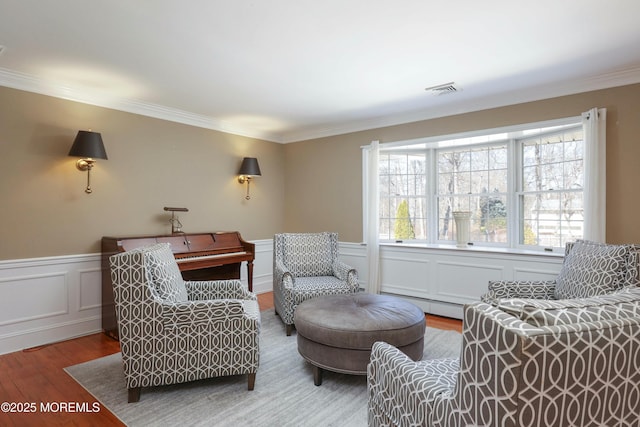 living area featuring a baseboard heating unit, visible vents, wood finished floors, and crown molding