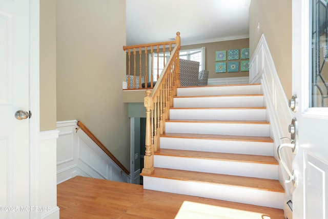 stairs with crown molding, a decorative wall, and a wainscoted wall