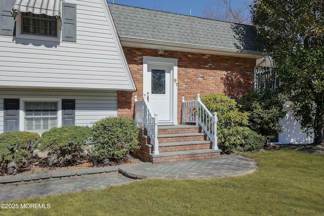 property entrance with brick siding, roof with shingles, and a lawn