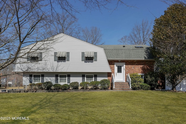 tri-level home featuring a front lawn, brick siding, a gambrel roof, and a shingled roof