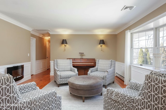 living area featuring visible vents, a glass covered fireplace, wood finished floors, wainscoting, and a baseboard radiator