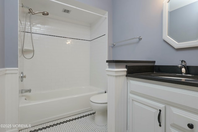 bathroom featuring vanity, a wainscoted wall, tile patterned flooring, shower / washtub combination, and toilet