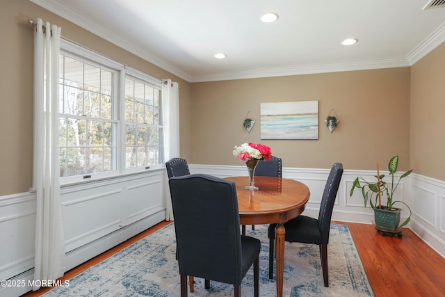 dining space with wainscoting, a baseboard heating unit, ornamental molding, and wood finished floors