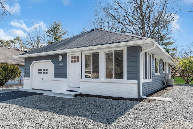 bungalow-style house with brick siding, an attached garage, a shingled roof, cooling unit, and driveway