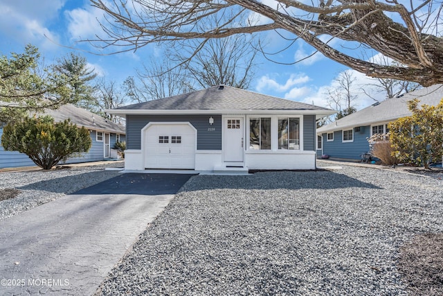 bungalow-style home with entry steps, aphalt driveway, an attached garage, a shingled roof, and brick siding