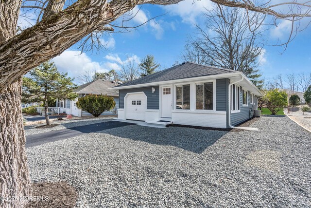 view of front of property with driveway, cooling unit, roof with shingles, an attached garage, and brick siding