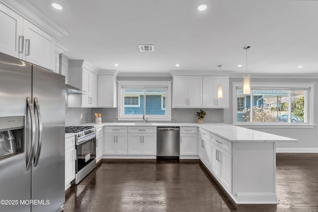 kitchen featuring visible vents, ornamental molding, stainless steel appliances, a peninsula, and wall chimney range hood