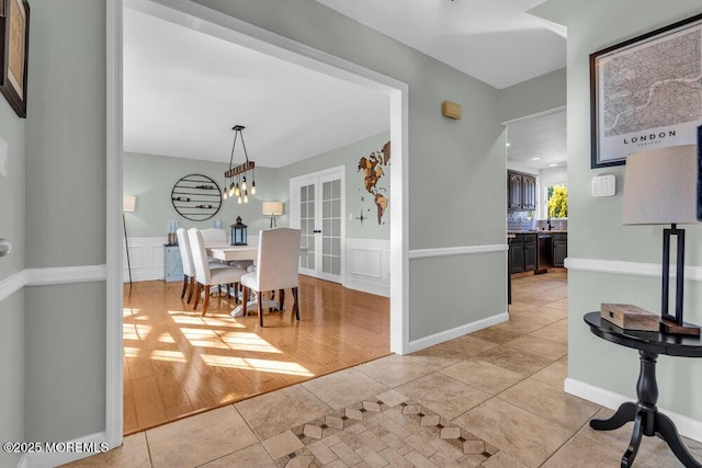 dining area featuring a decorative wall, light tile patterned flooring, french doors, and wainscoting