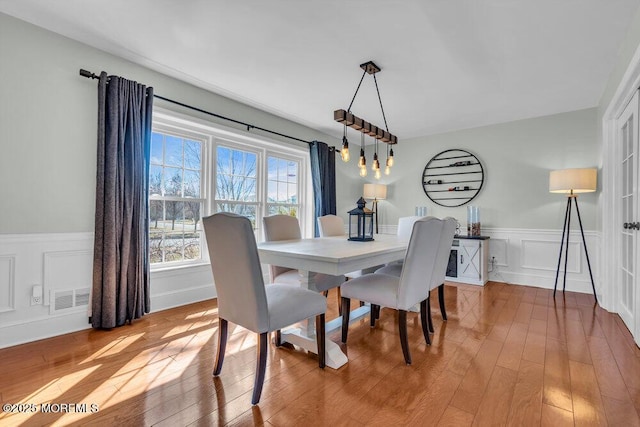 dining space featuring visible vents, a decorative wall, wainscoting, and hardwood / wood-style flooring