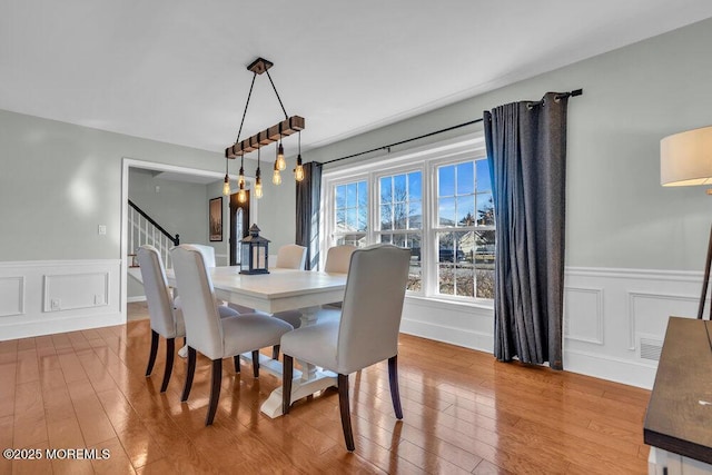 dining area with a decorative wall, wainscoting, stairs, and wood finished floors