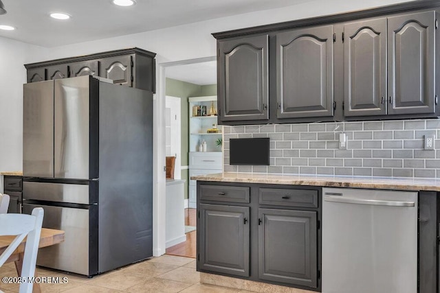 kitchen with light tile patterned floors, stainless steel appliances, light stone countertops, and backsplash