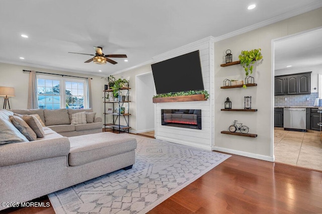 living area with light wood finished floors, ceiling fan, ornamental molding, recessed lighting, and a glass covered fireplace