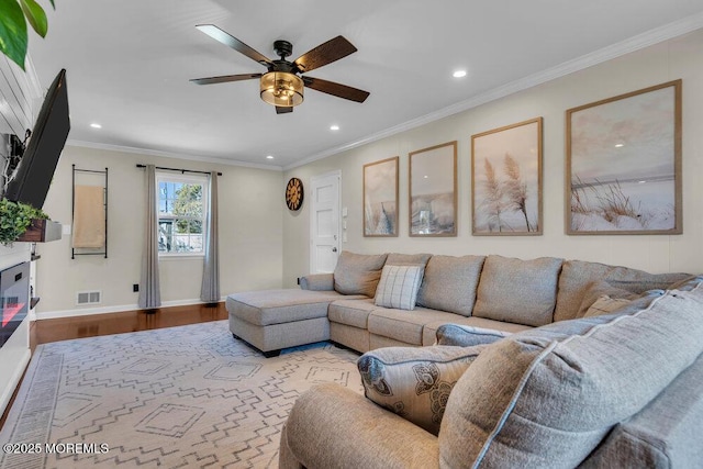 living room with visible vents, ornamental molding, wood finished floors, baseboards, and ceiling fan