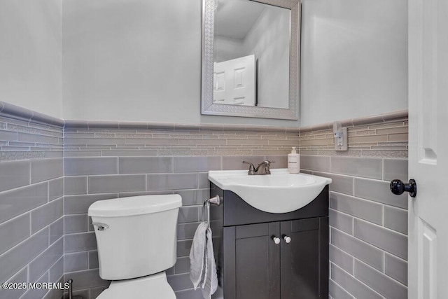 bathroom featuring a wainscoted wall, toilet, tile walls, and vanity