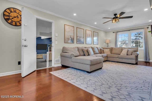 living area with visible vents, wood finished floors, baseboards, and ornamental molding