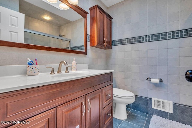 bathroom featuring tile patterned flooring, visible vents, vanity, tiled shower, and tile walls