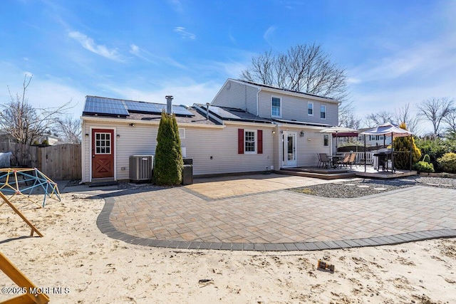 back of house featuring outdoor dining space, central AC unit, fence, a wooden deck, and roof mounted solar panels