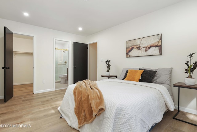 bedroom featuring light wood finished floors, a spacious closet, and baseboards