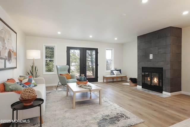 living room with baseboards, light wood finished floors, recessed lighting, a tile fireplace, and french doors