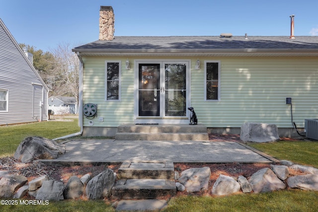 rear view of house with a lawn, entry steps, a chimney, and roof with shingles